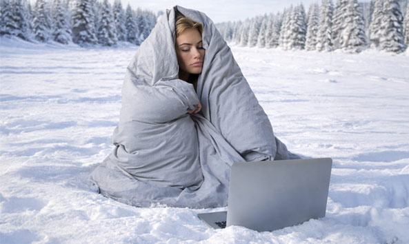 Person wrapped in a blanket in the snow with a laptop.